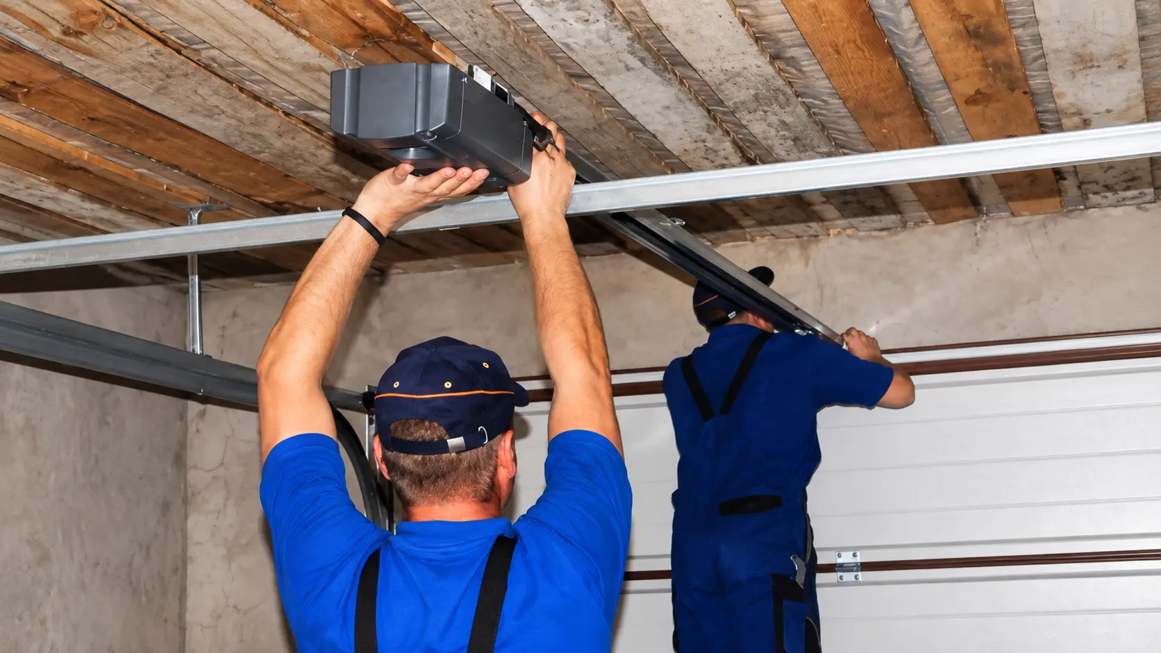 Two technicians installing garage door opener equipment and rail hardware