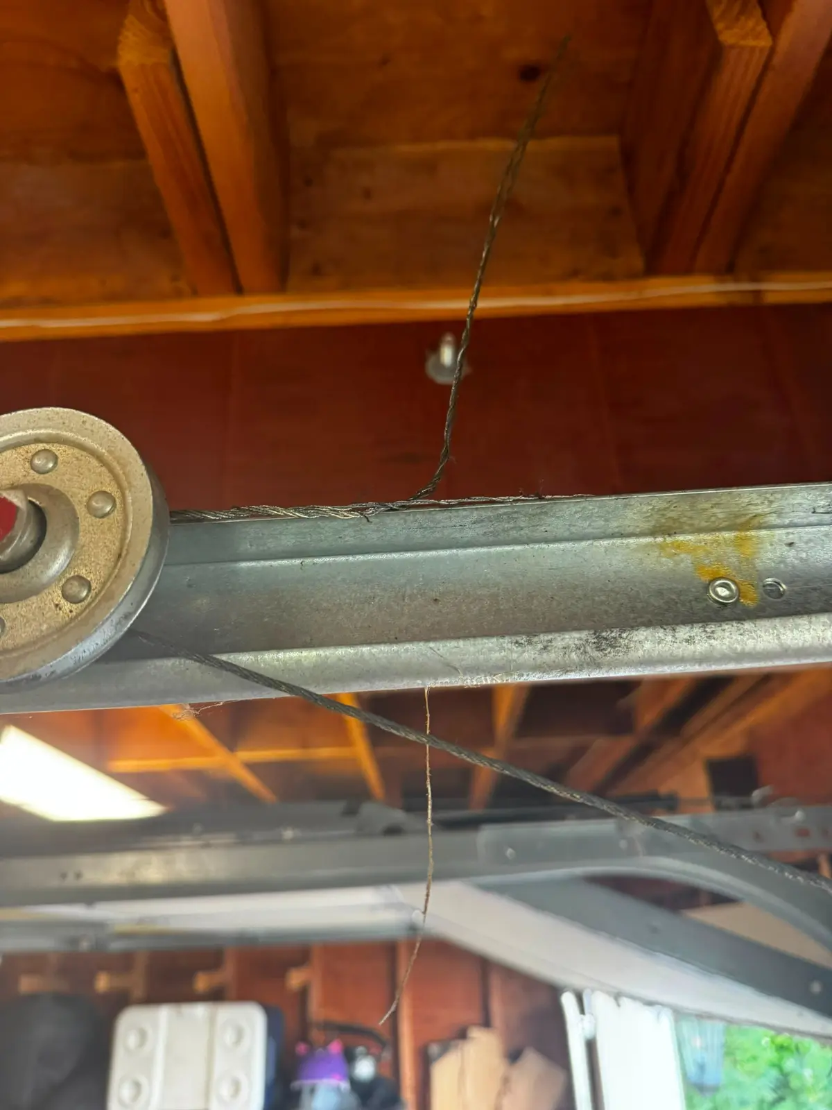 Frayed garage door lift cable strands visible near the overhead track and roller